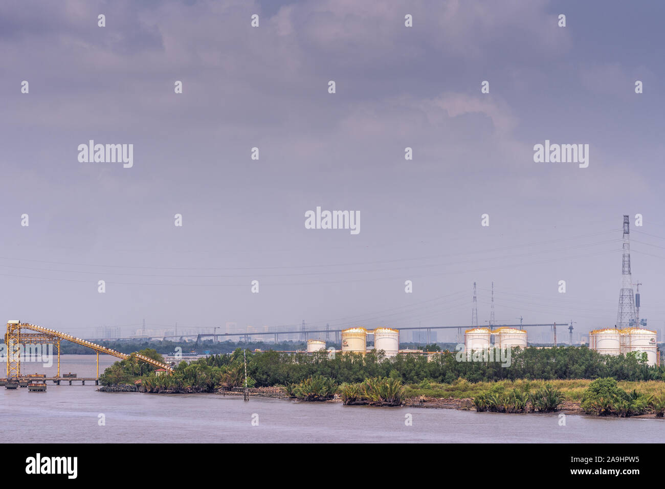 Lungo il fiume Tau, Vietnam - Marzo 12, 2019: Phuoc Khanh area. PetroVietnam serbatoi bianco fronteggiata da fogliame verde e giallo pipeline sistema di pompaggio su wa Foto Stock