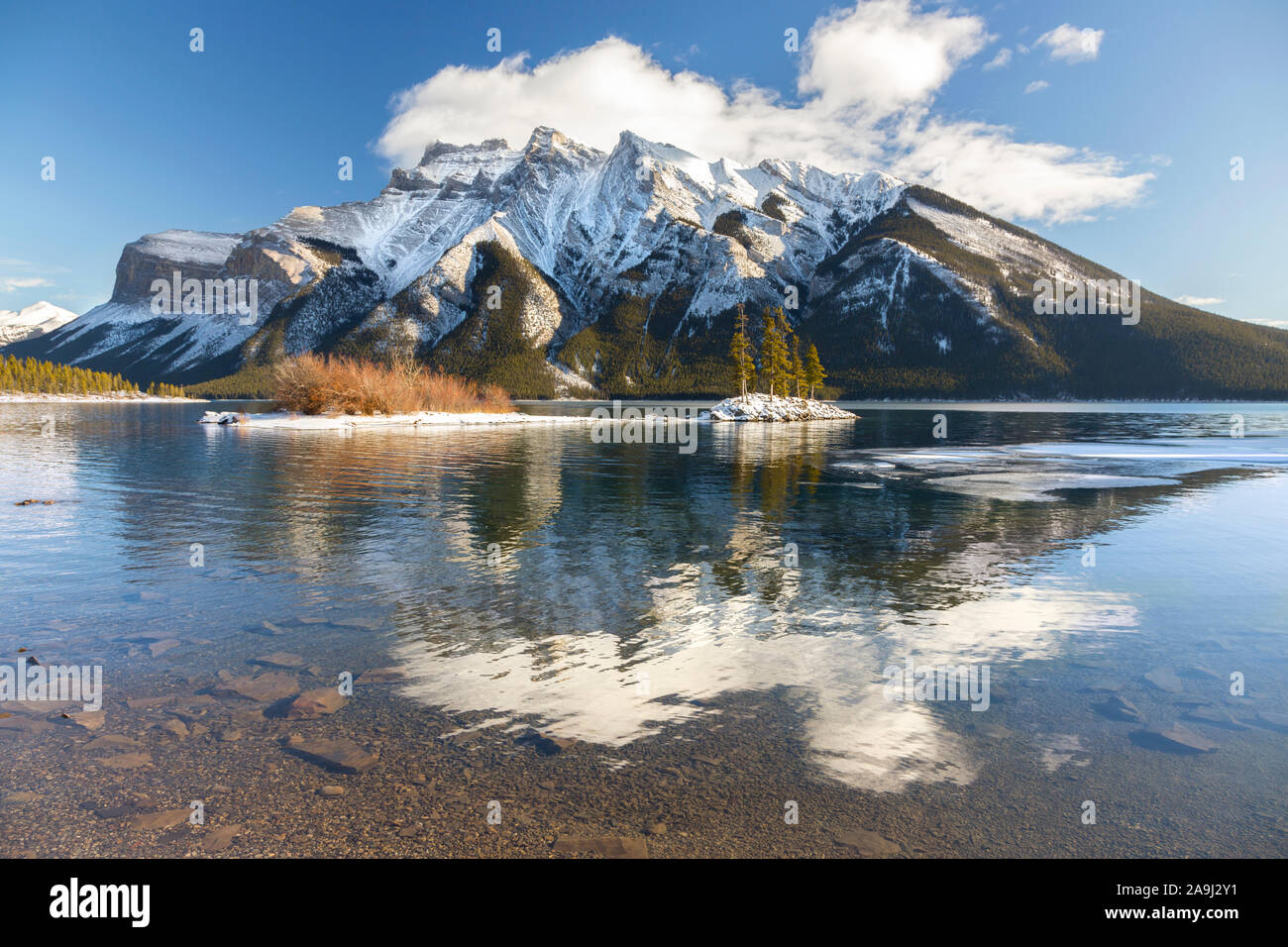 Paesaggio delle vette innevate con nube bassa riflessa in acque calme. Splendido lago Minnewanka, Banff National Park, Alberta, Canadian Rockies Foto Stock