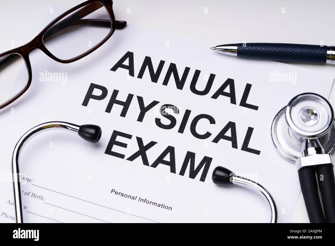 Elevato angolo di vista fisico annuale forma di esame con uno stetoscopio e occhiali sulla scrivania bianca Foto Stock