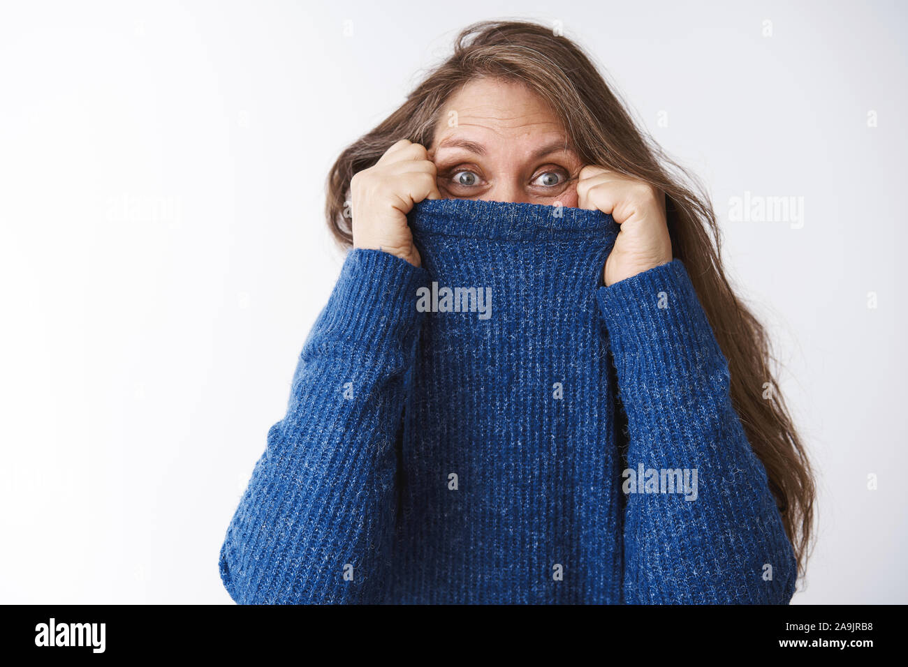 La donna si nasconde in un maglione, ingannare intorno a. Gioioso ed eccitato donna di mezza età baby giocare i ragazzi pieghevole tirando il collare sulla faccia e spiata un Foto Stock