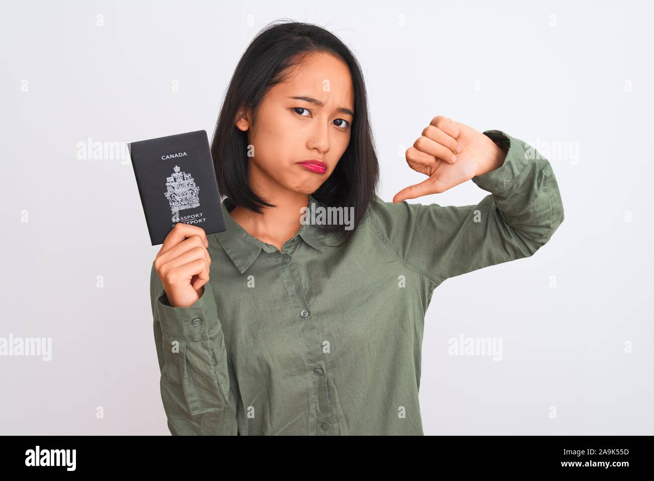 Bella donna cinese holding Canada passaporto canadese isolato su sfondo bianco con volto arrabbiato, segno negativo che mostra antipatia con i pollici dow Foto Stock
