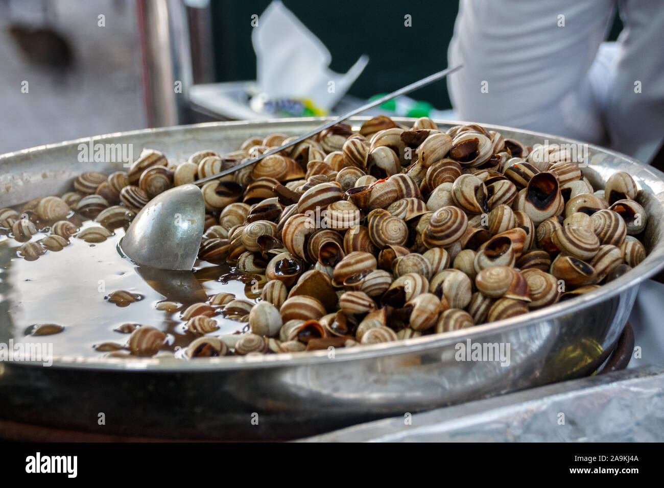 Padella con le lumache cucinate su un mercato nel souk di Marrakech Foto Stock
