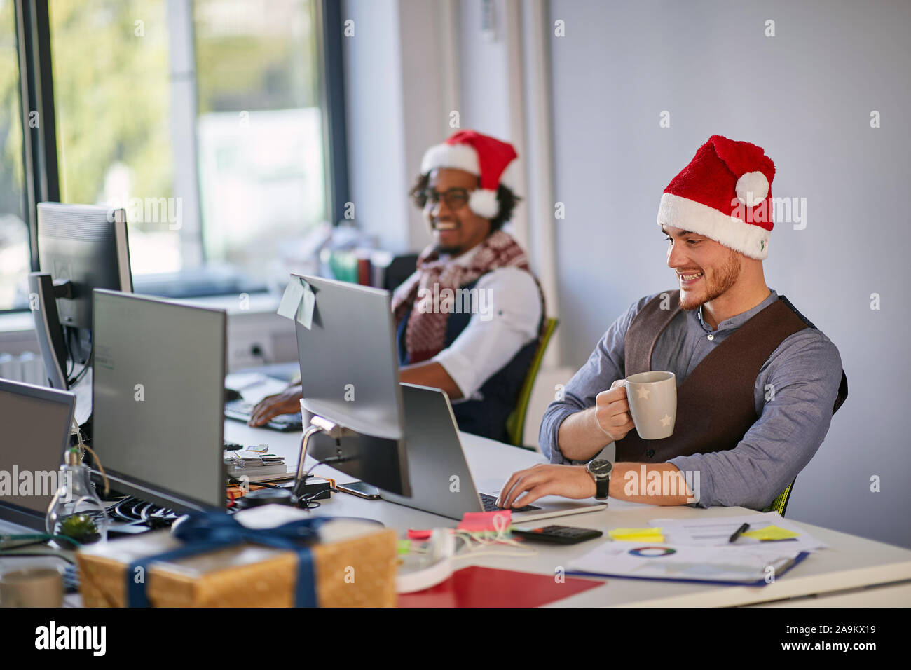 Giovane imprenditore sorridente in santa hat lavorando a un computer a Natale presso l'azienda. Foto Stock