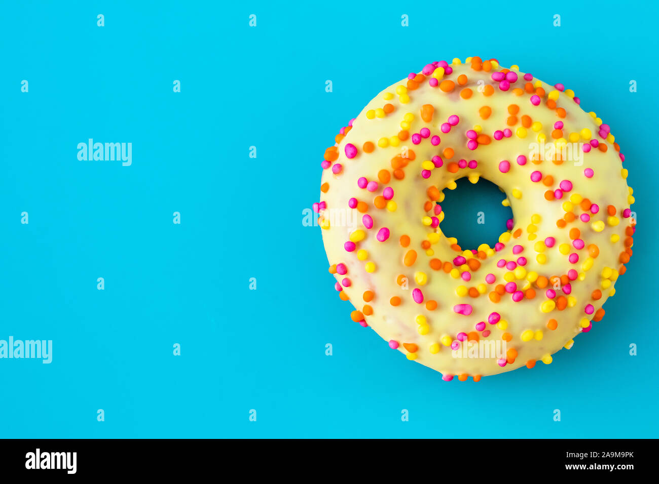 Ciambella di colore giallo su sfondo blu con una copia dello spazio. Topping multicolore su smalto di colore giallo. Malsana alto-caloria cibo. Foto Stock