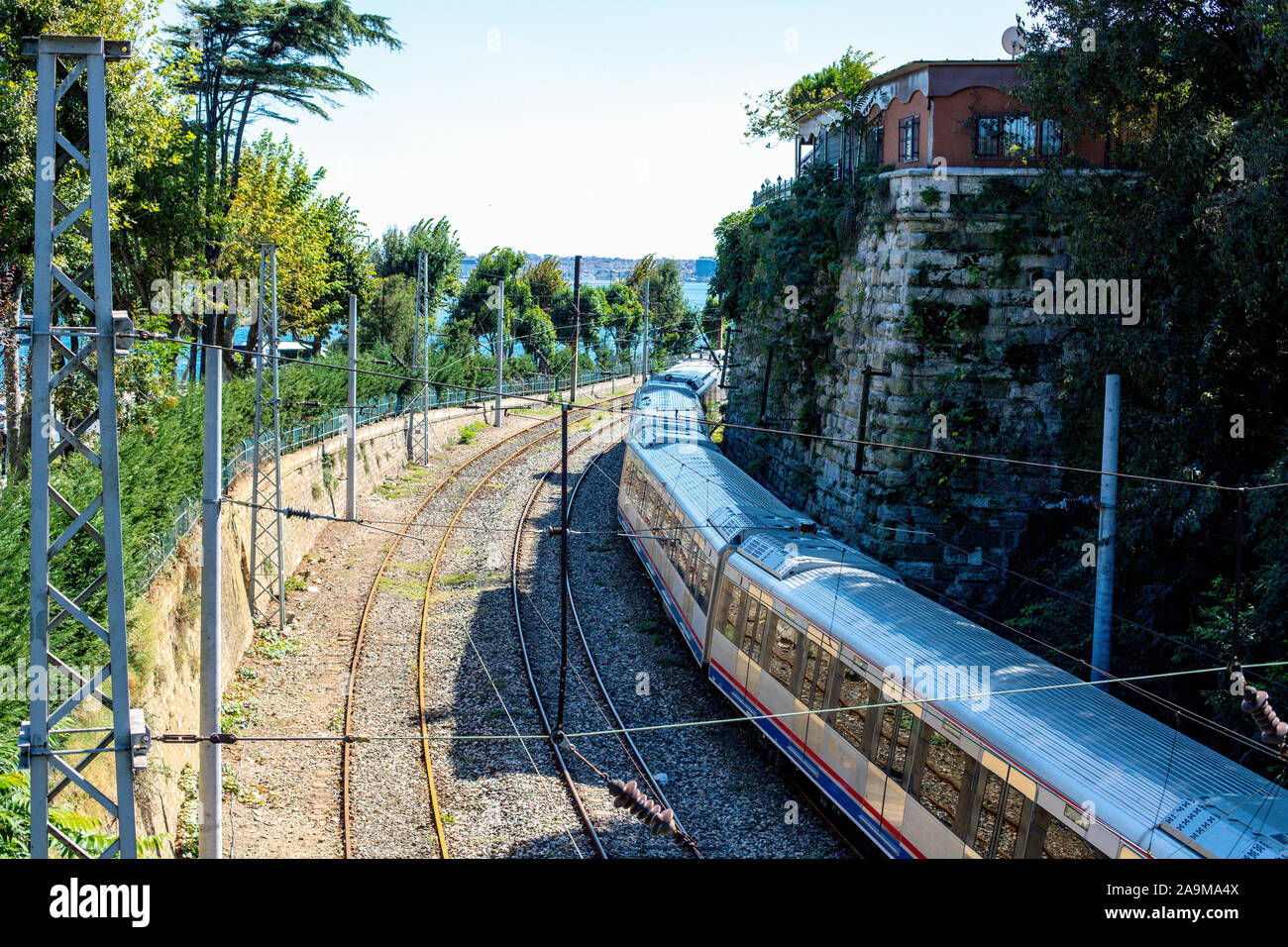 La stazione ferroviaria si volge verso il mare. Treno sulla linea ferroviaria con vista mare. Un treno tra il verde degli alberi e il muro di pietre. Foto Stock