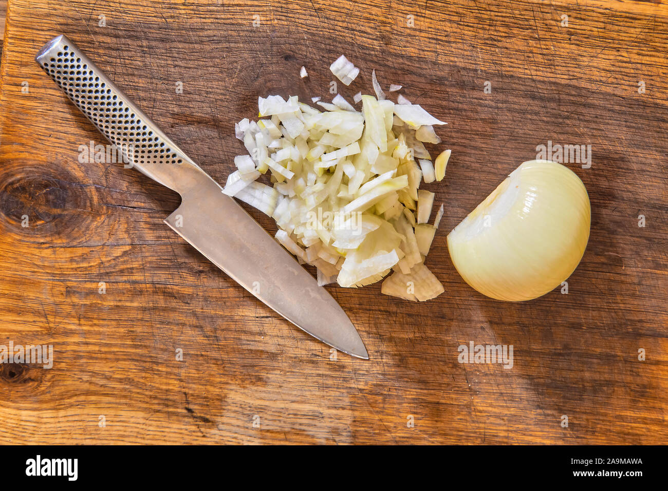 Tagliate a fette le cipolle a dadini su un tagliere di legno con un coltello di cuochi e una metà o metà bianco Sbucciate la cipolla di cottura Foto Stock