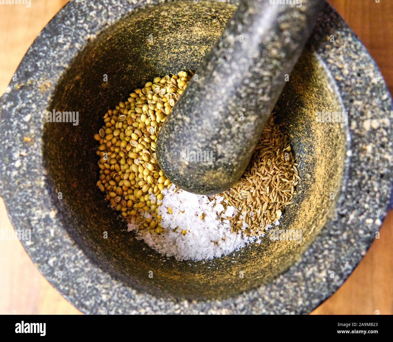Close up di cumino e semi di coriandolo con sale marino fiocchi in granito di un mortaio e pestello Foto Stock