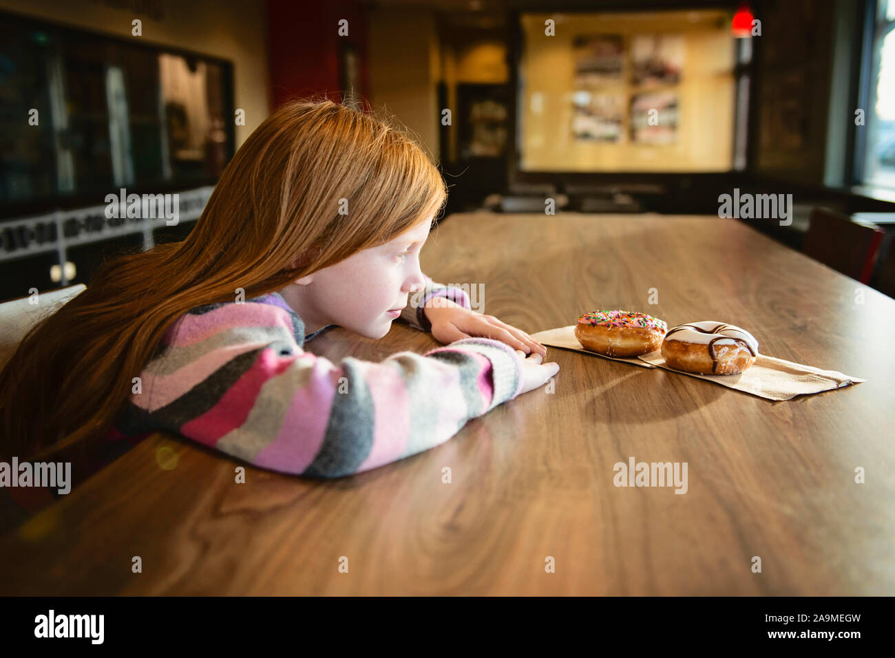 Rosso giovane ragazza dai capelli cercando longingly a deliziose ciambelle Foto Stock