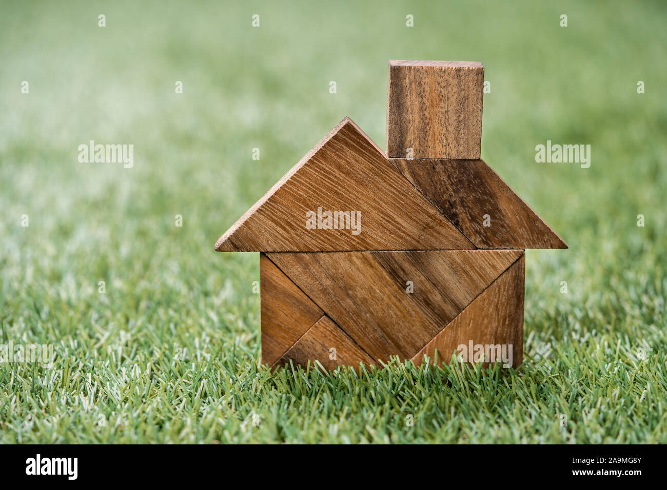 Angolo di Alta Vista di Tangram Puzzle a forma di casa su artificiali erba verde sullo sfondo Foto Stock