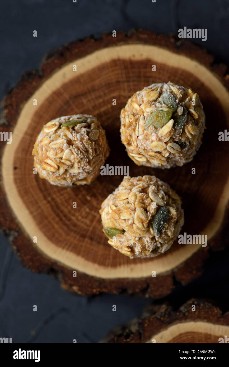 Cibo Vegan concetto. Close up congelati Fiocchi d'avena e le sfere di energia con i semi di zucca in legno di rovere e lastra su sfondo nero in vista dall'alto uno spazio di copia Foto Stock