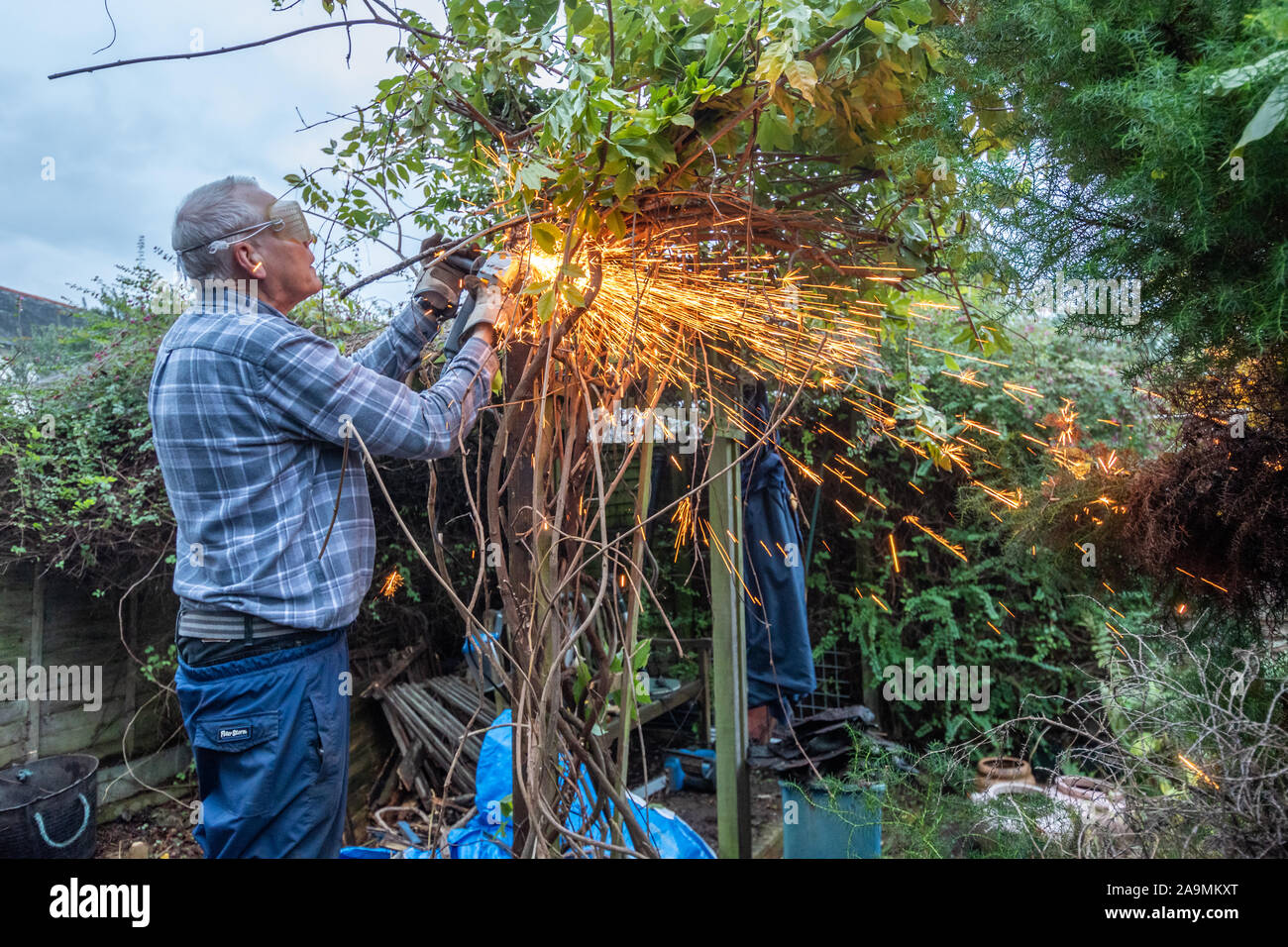 L'uomo utilizzando una smerigliatrice angolare lavora in giardino con scintille volanti. Il taglio di pericoloso vecchi chiodi da un post. Foto Stock