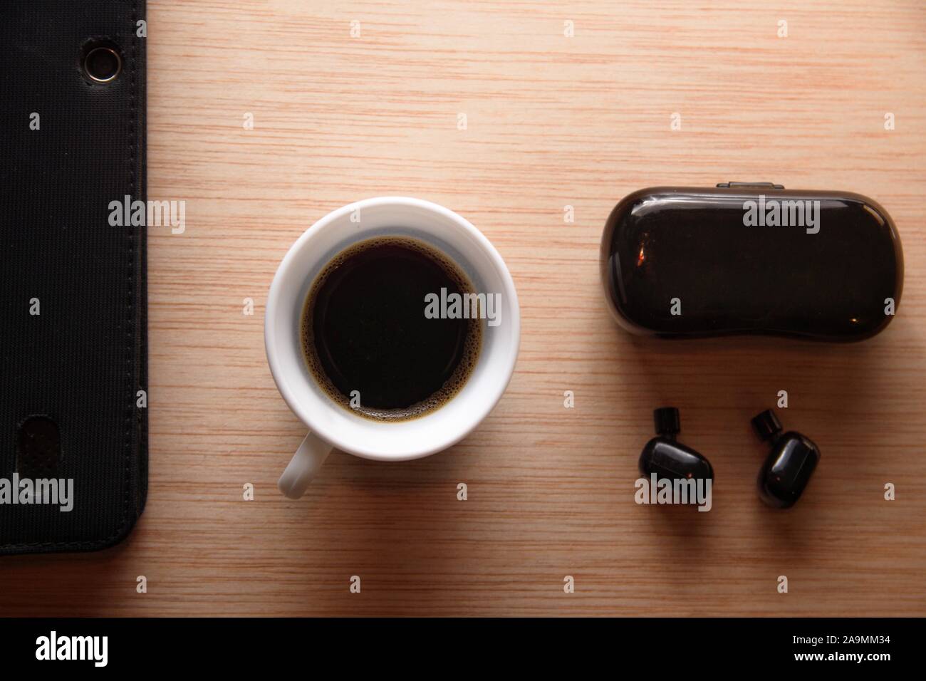 Gli auricolari Bluetooth accanto ad un mobile e una tazza di caffè su una scrivania in legno. Disposizione piatta con copia vuota dello spazio. Foto Stock