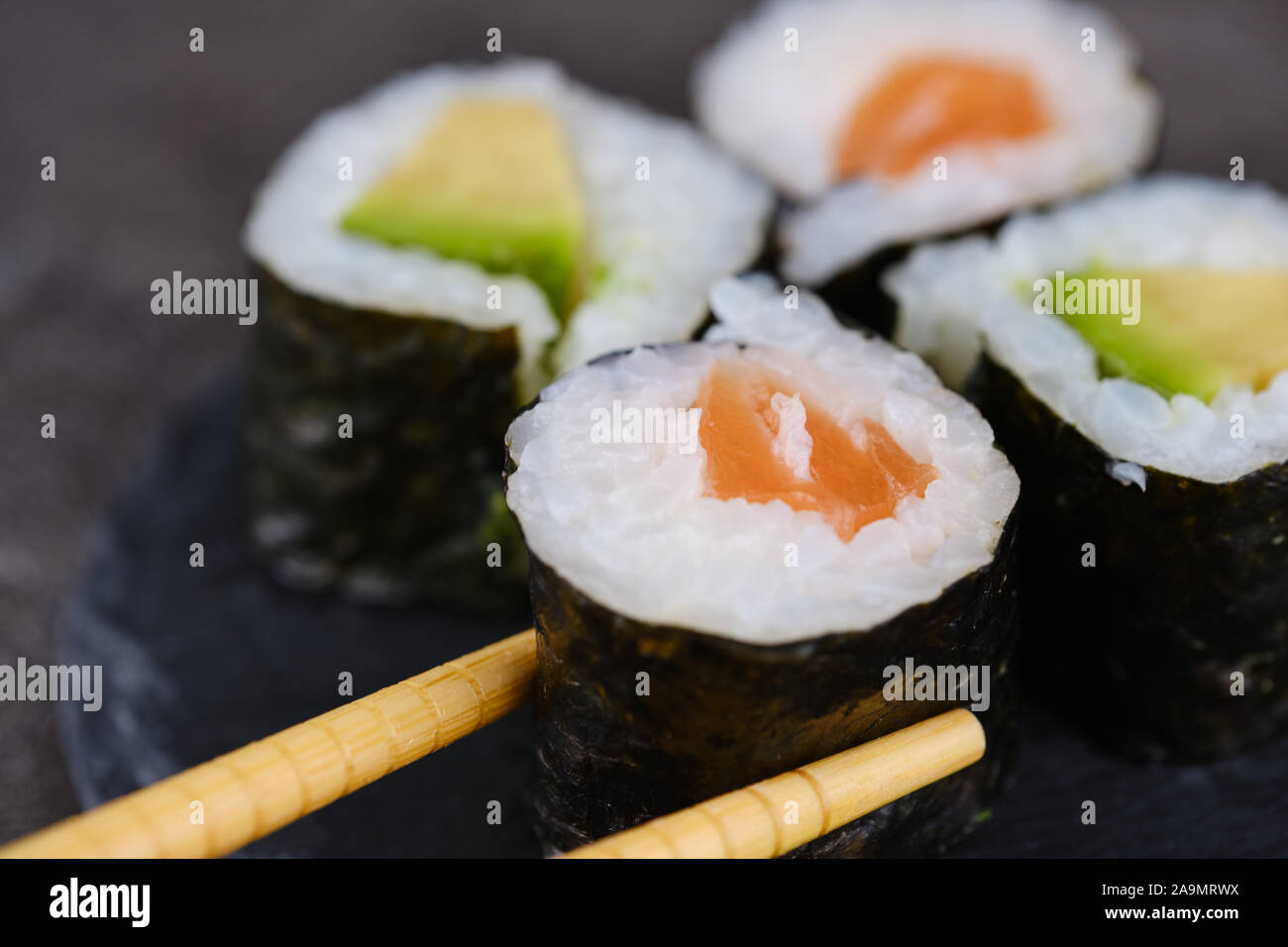 Sake Giapponese maki roll con salmone e avocado, bacchette di legno tenendo un rotolo Foto Stock