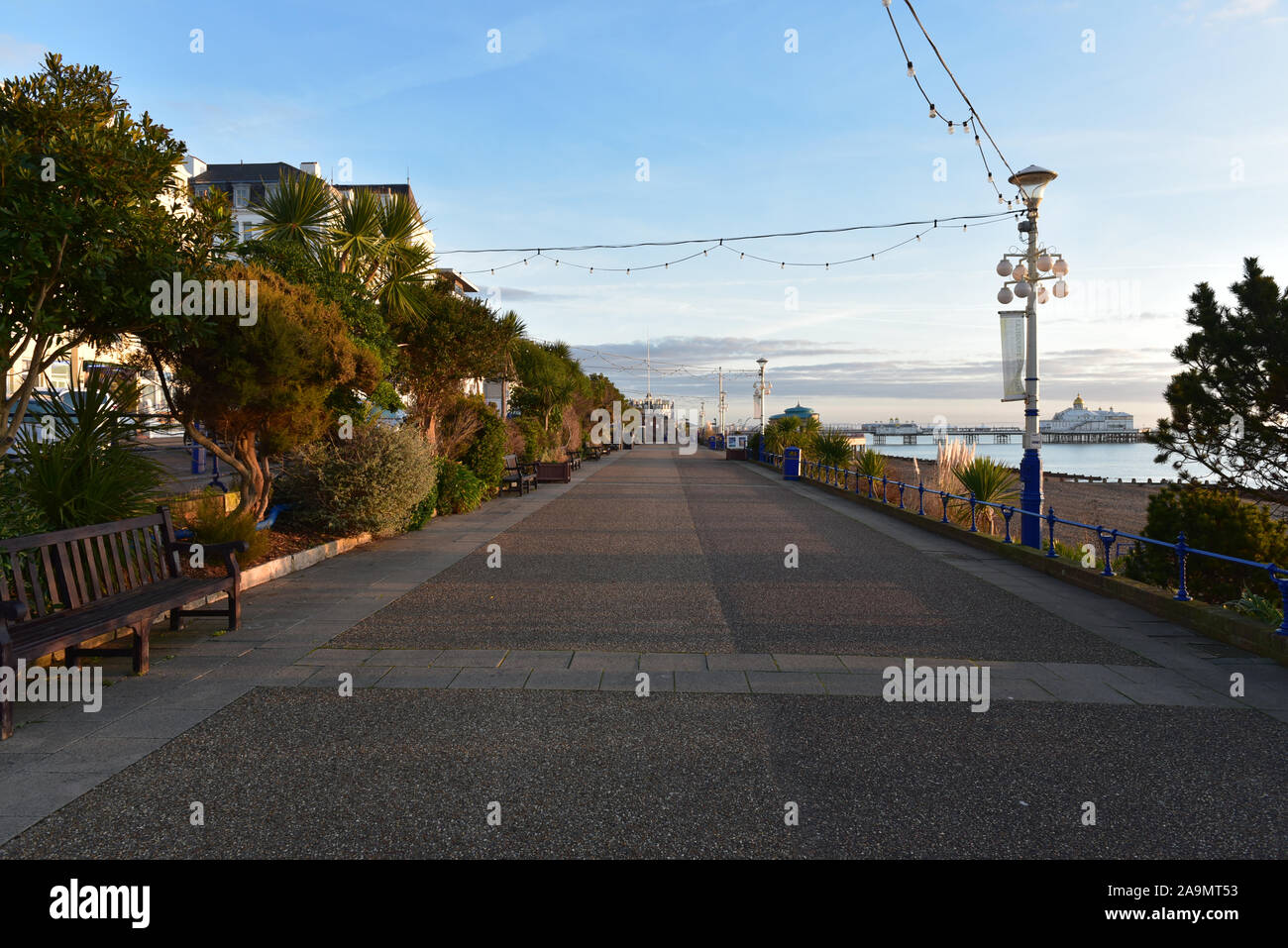 Svuotare il lungomare con panca, lampada posta e Eastbourne Pier a distanza sotto un cielo alba Foto Stock