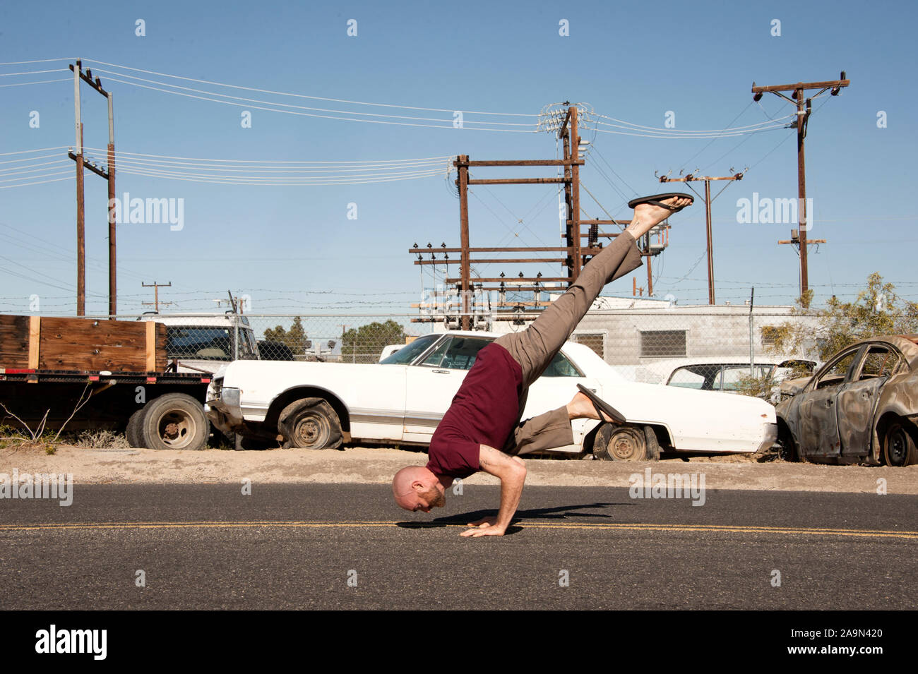 L uomo nella sua anni trenta con la barba a praticare yoga da una vecchia auto junkyard nel deserto. Foto Stock