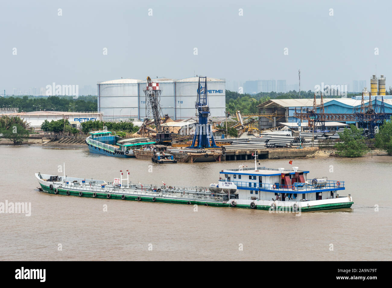 Lungo il fiume Tau, Vietnam - Marzo 12, 2019: Dong Thap 09 fiume vele introduttore su acqua marrone nella parte anteriore di Phuoc Khanh porta di petrolio che mostra le cisterne, pipeline Foto Stock