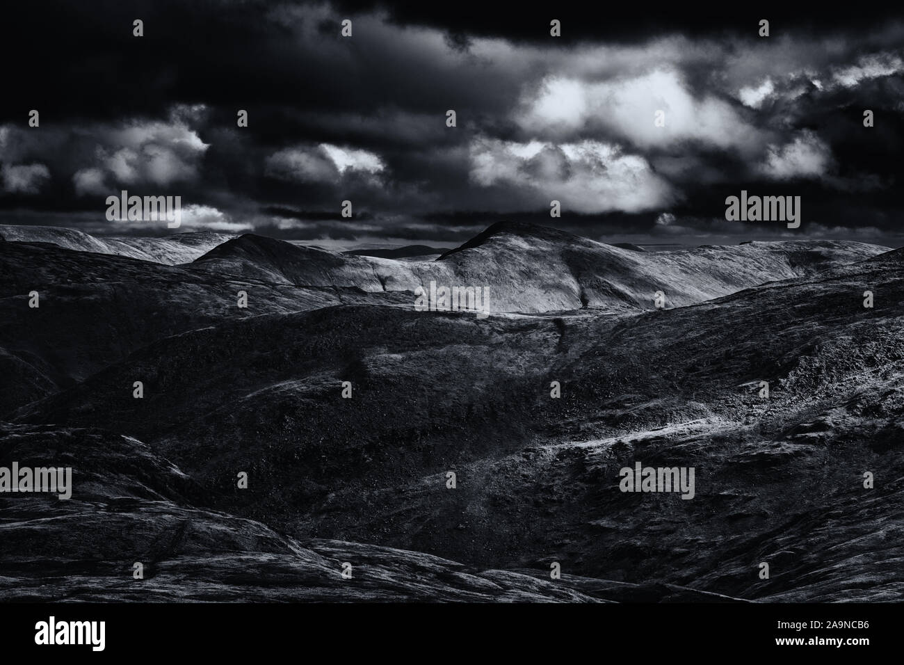 Patchy luce solare su scenic mountain range in autunno nel Parco Nazionale del Distretto dei Laghi, UK - monocromatico modifica Foto Stock
