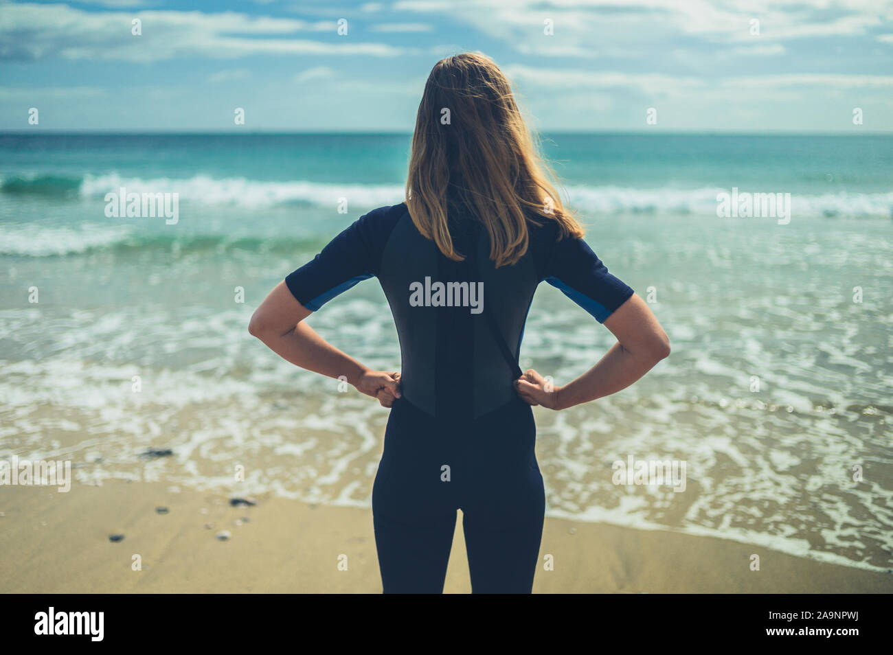 Una giovane donna che indossa una muta in piedi sulla spiaggia in estate Foto Stock