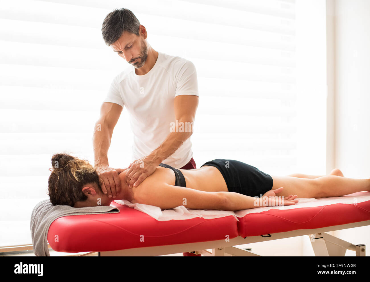 L'uomo osteopata massaggiare i suoi pazienti trapezio muscoli mentre una donna recante sul suo ventre un lettino in un ufficio medici Foto Stock