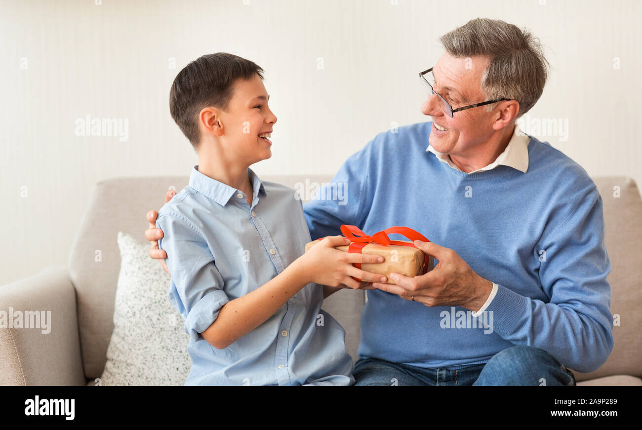 Ragazzo dando nonno regalo di compleanno seduto sul divano Indoor Foto Stock