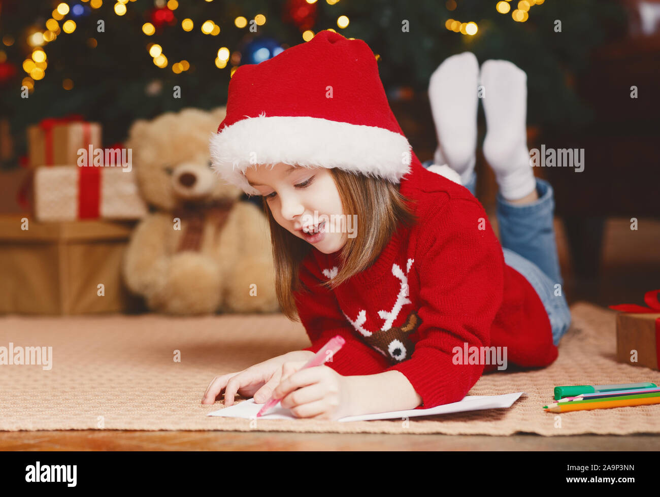 Trasognata bambina scrivere lettera a Babbo sotto albero di natale Foto Stock