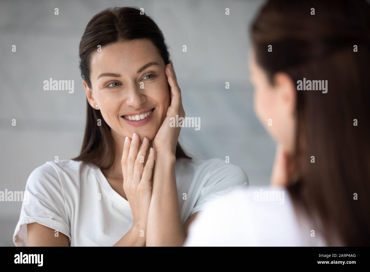 Felice giovane e bella signora di toccare la faccia guardare nello specchio del bagno Foto Stock