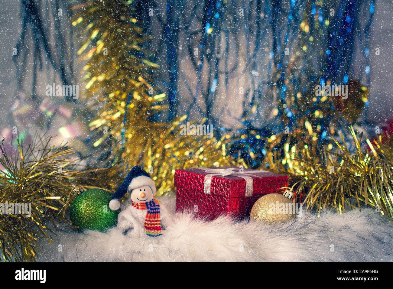 Un sorridente pupazzo di neve in una sciarpa accanto a doni e giocattoli di Natale sullo sfondo di tinsel e neve. Un po' di pupazzo di neve è in piedi in pelliccia. Foto Stock