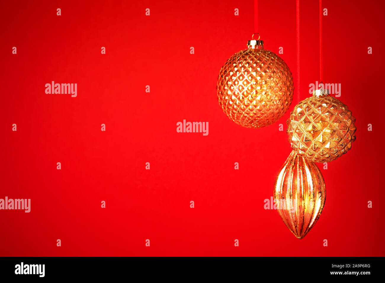 Tre golden baubles di Natale appeso contro lo sfondo rosso. Anno nuovo bigliettino. Messa a fuoco selettiva. Foto Stock