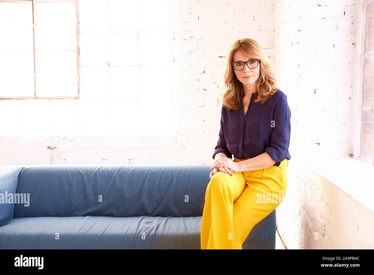 Ritratto di eleganti donna di mezza età guardando la fotocamera e sorridenti mentre vi rilassate sul divano. Foto Stock
