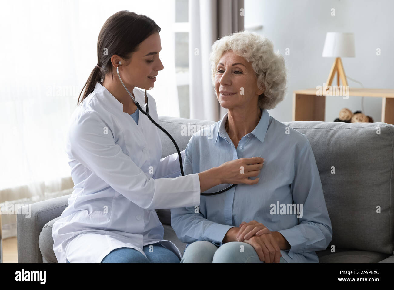 Giovane donna medico tenendo uno stetoscopio esaminando senior nonna paziente Foto Stock
