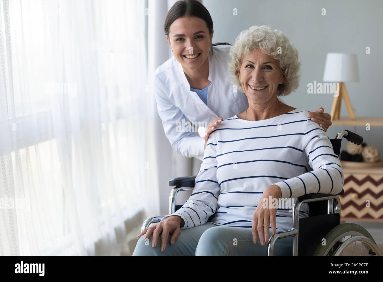 Felice la nonna disabili su sedia a rotelle e infermiere guardare fotocamera Foto Stock