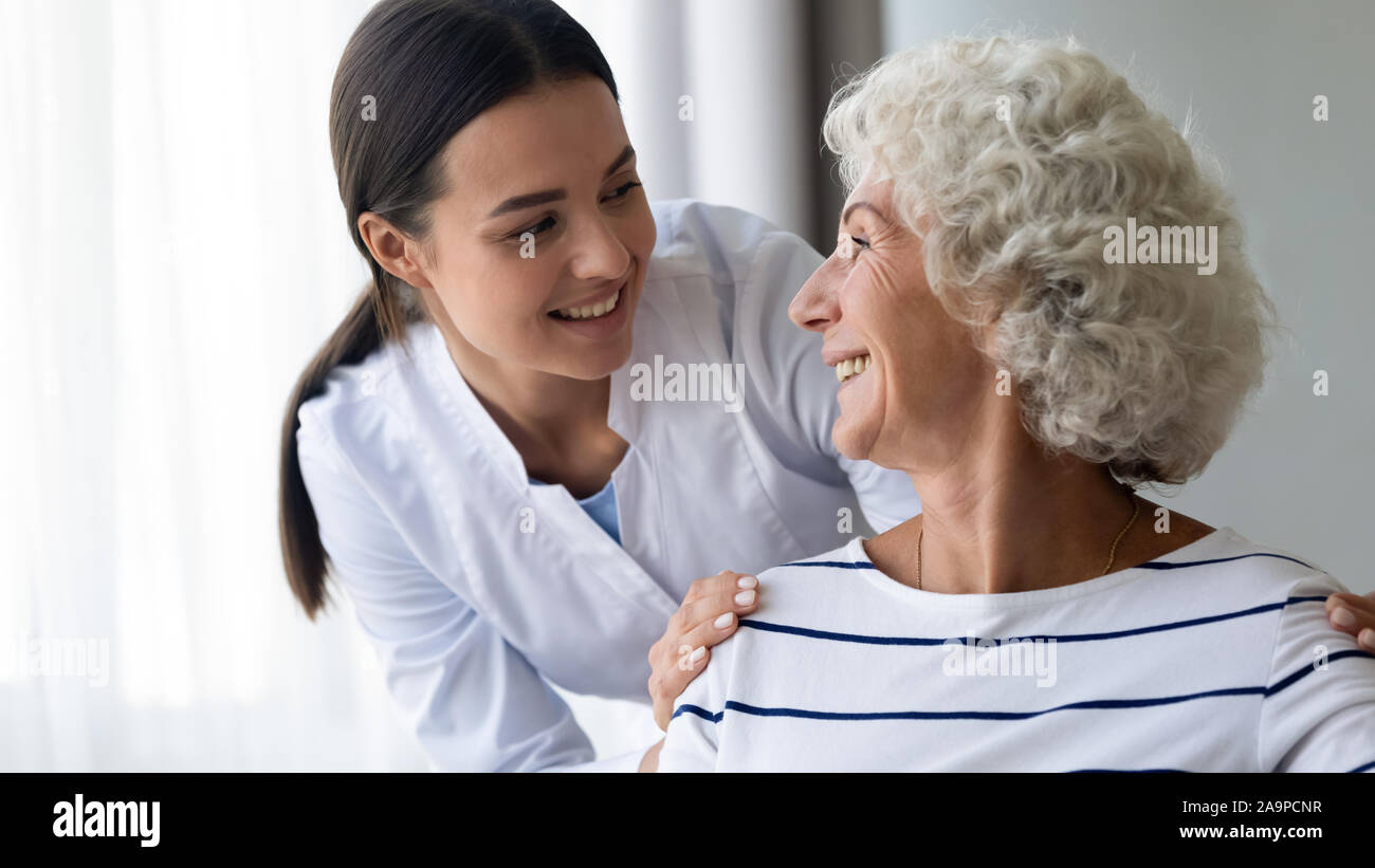 Caring sorridente giovane infermiere avendo cura di sambuco nonna paziente Foto Stock