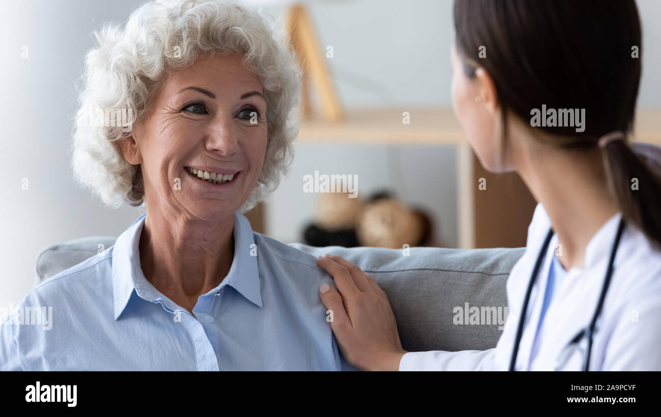 Nonna felice guardando il giovane infermiere aiutando supporto paziente vecchio Foto Stock