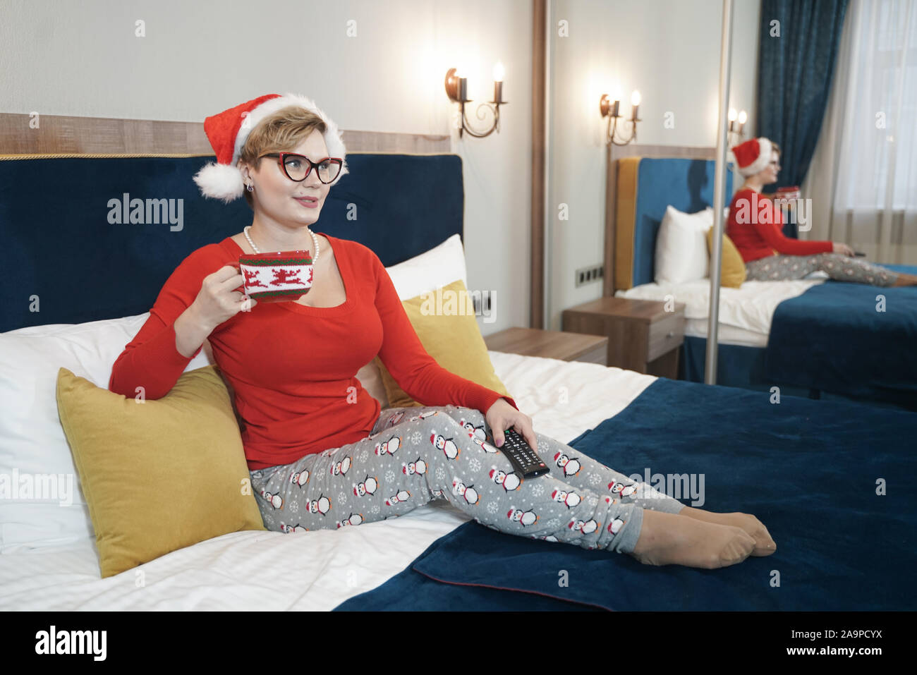 Giovane donna in rosso maglione di natale guardando la TV sul letto da solo Foto Stock