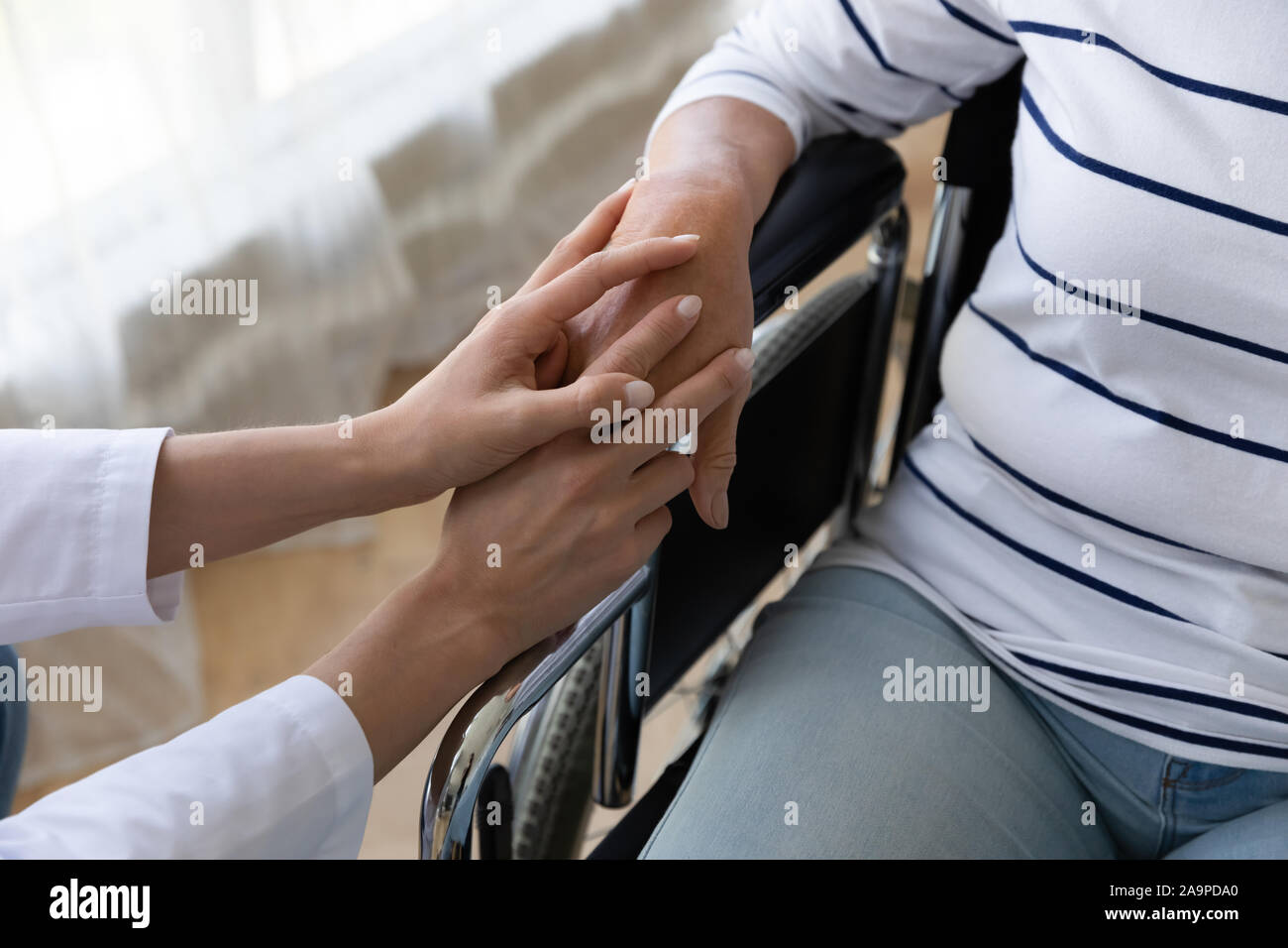 L'infermiera tenere il supporto a mano handicappati senior paziente su sedia a rotelle, primo piano Foto Stock