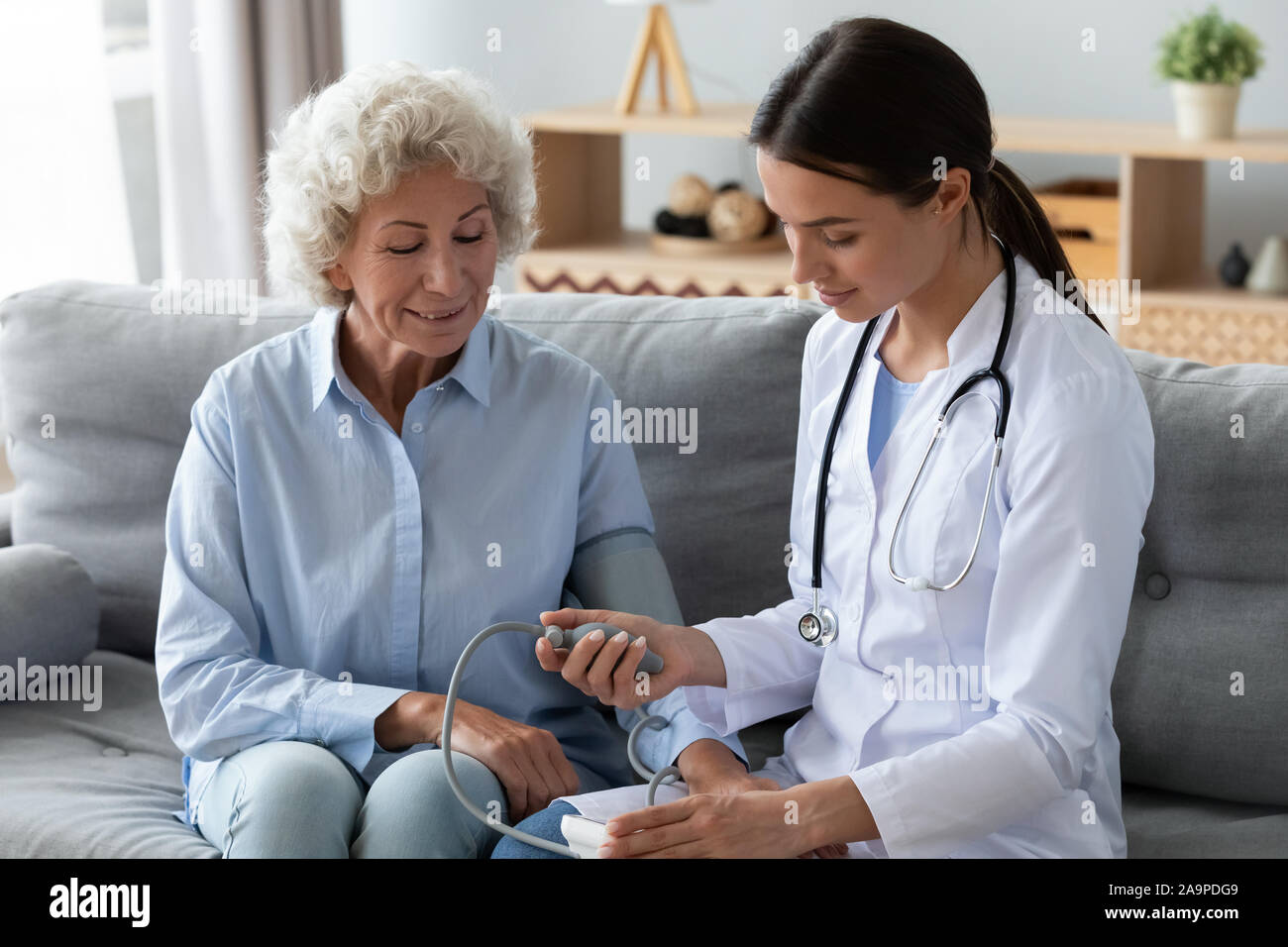 Femmina giovane infermiere di misurare la pressione sanguigna controllare la vecchia nonna paziente Foto Stock