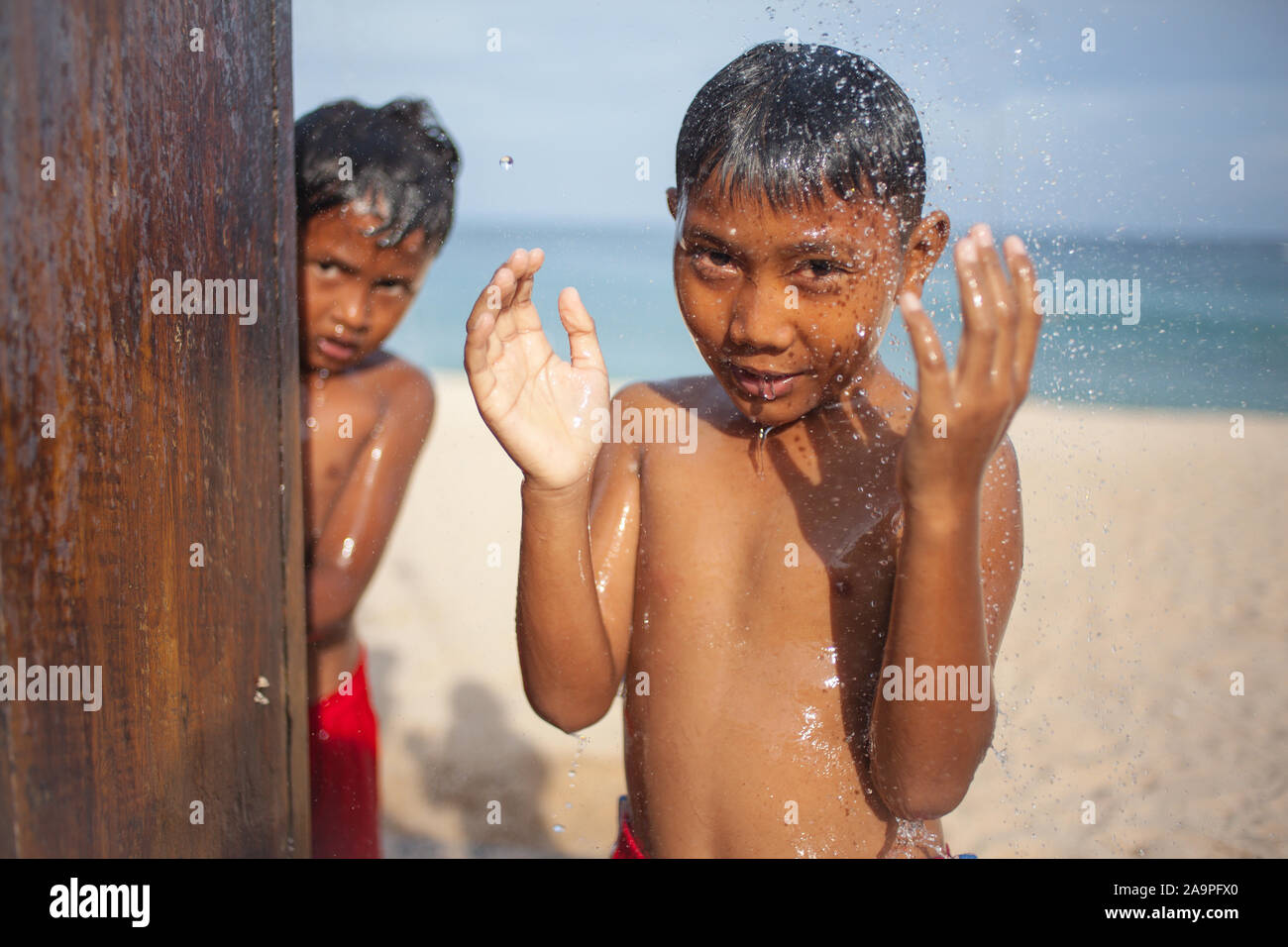Sanur, Bali Indonesia - 22 febbraio 2013. Ritratto di ragazzi piccoli tenendo doccia sulla spiaggia, bambina carina con piacere rinfrescante in acqua fredda Foto Stock