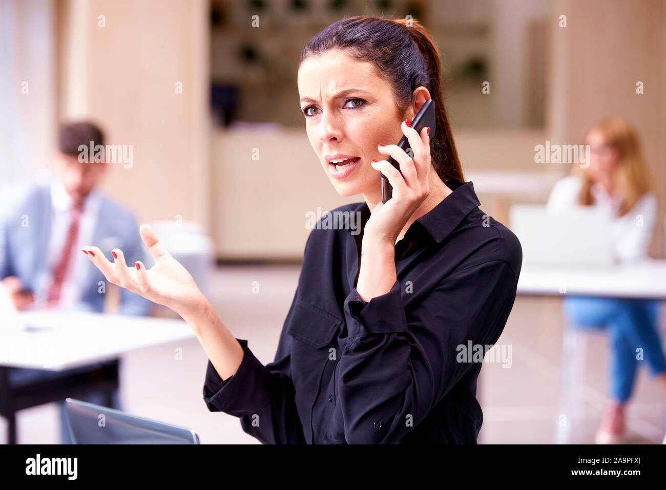 Colpo di sottolineato imprenditrice parlando con qualcuno sul suo telefono cellulare mentre in piedi in ufficio. Foto Stock