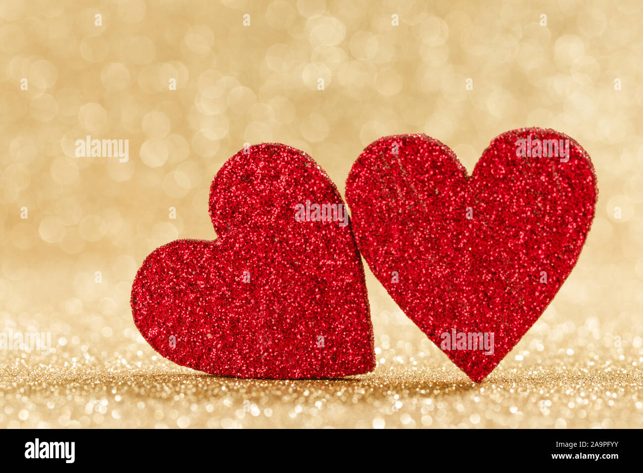 Due piccoli fatti a mano glitter rosso cuori in bright golden lights sfondo bokeh Valentines Day card Foto Stock