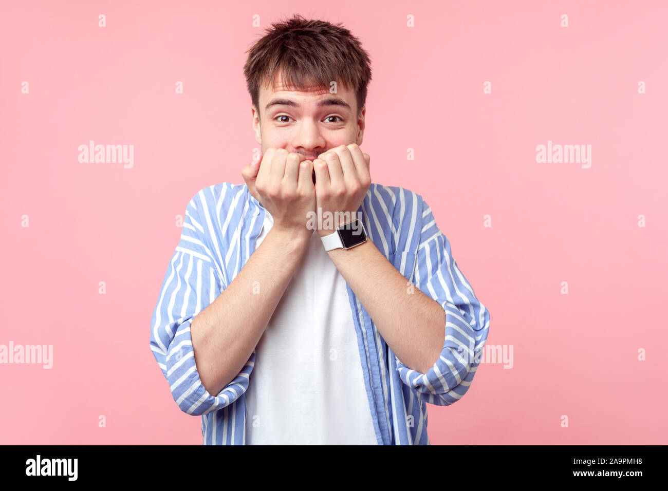 Ritratto di coward, nervoso spaventato i capelli castani uomo nel casual camicia a righe di mordere le unghie delle dita, guardando la fotocamera con il terrore paura expressio Foto Stock