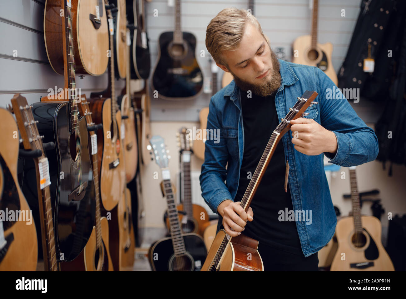 Barbuto giovane scegliendo una chitarra in music store Foto Stock