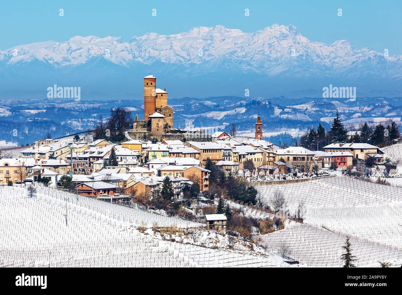 Piccola città medievale e vigneti sulle colline coperte di neve come le montagne sullo sfondo in Piemonte, Italia settentrionale. Foto Stock