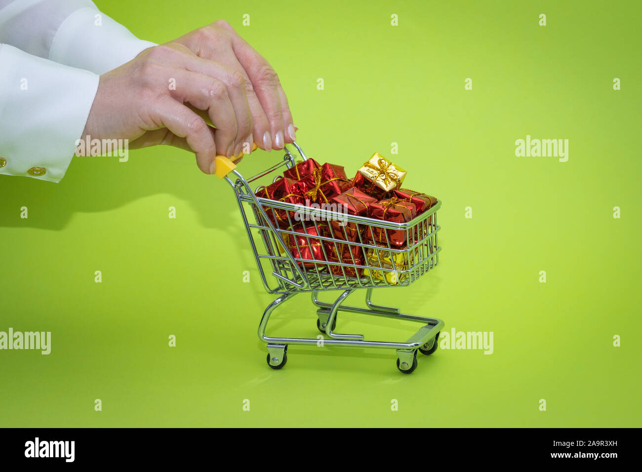 Mini carrello della spesa pieno di presenta su sfondo verde. Shopping di Natale concept Foto Stock