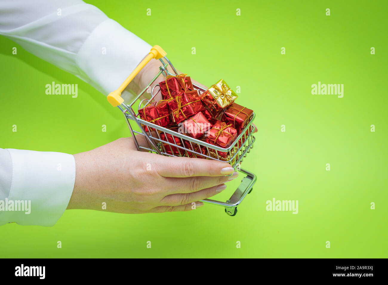 Mini carrello della spesa pieno di presenta su sfondo verde. Shopping di Natale concept Foto Stock