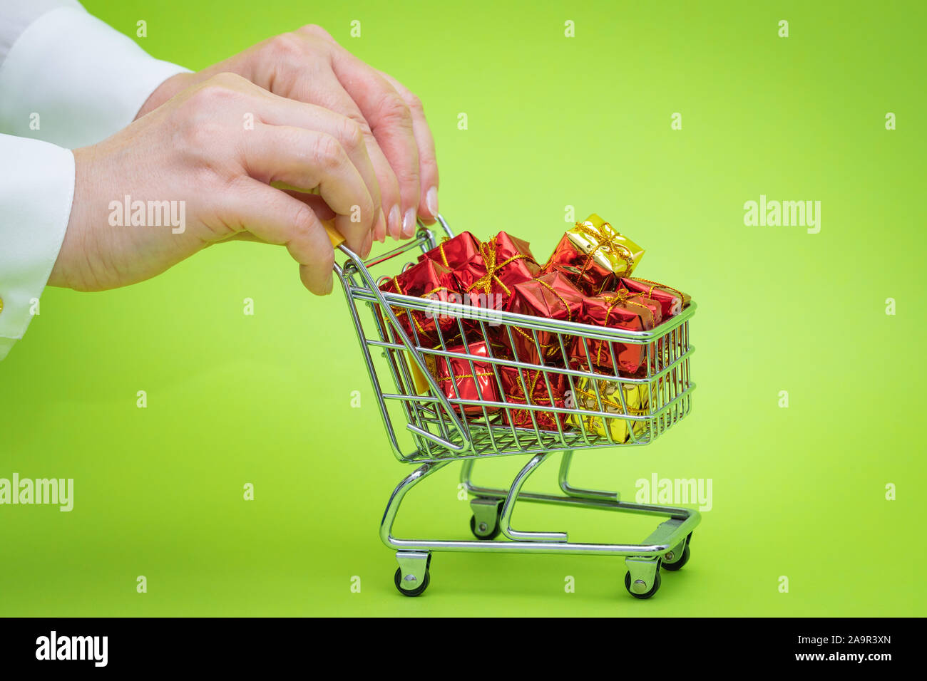 Mini carrello della spesa pieno di presenta su sfondo verde. Shopping di Natale concept Foto Stock