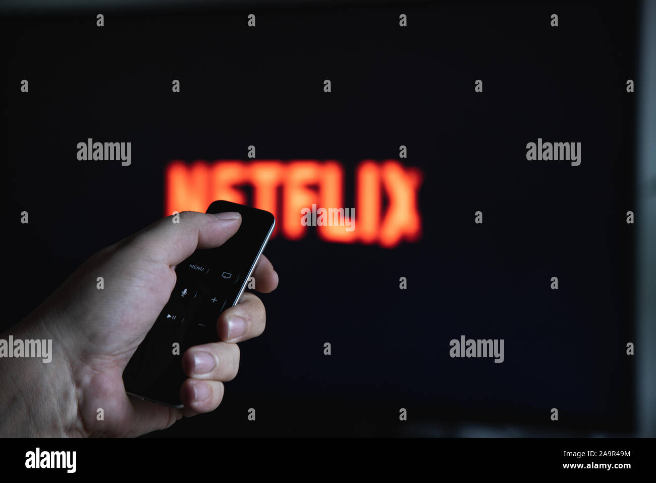 Chiusura del telecomando di Apple TV in mano e schermo TV con sfocati Logo Netflix Foto Stock