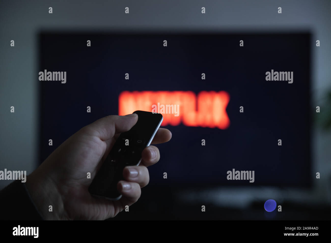 Chiusura del telecomando di Apple TV in mano e schermo TV con sfocati Logo Netflix Foto Stock