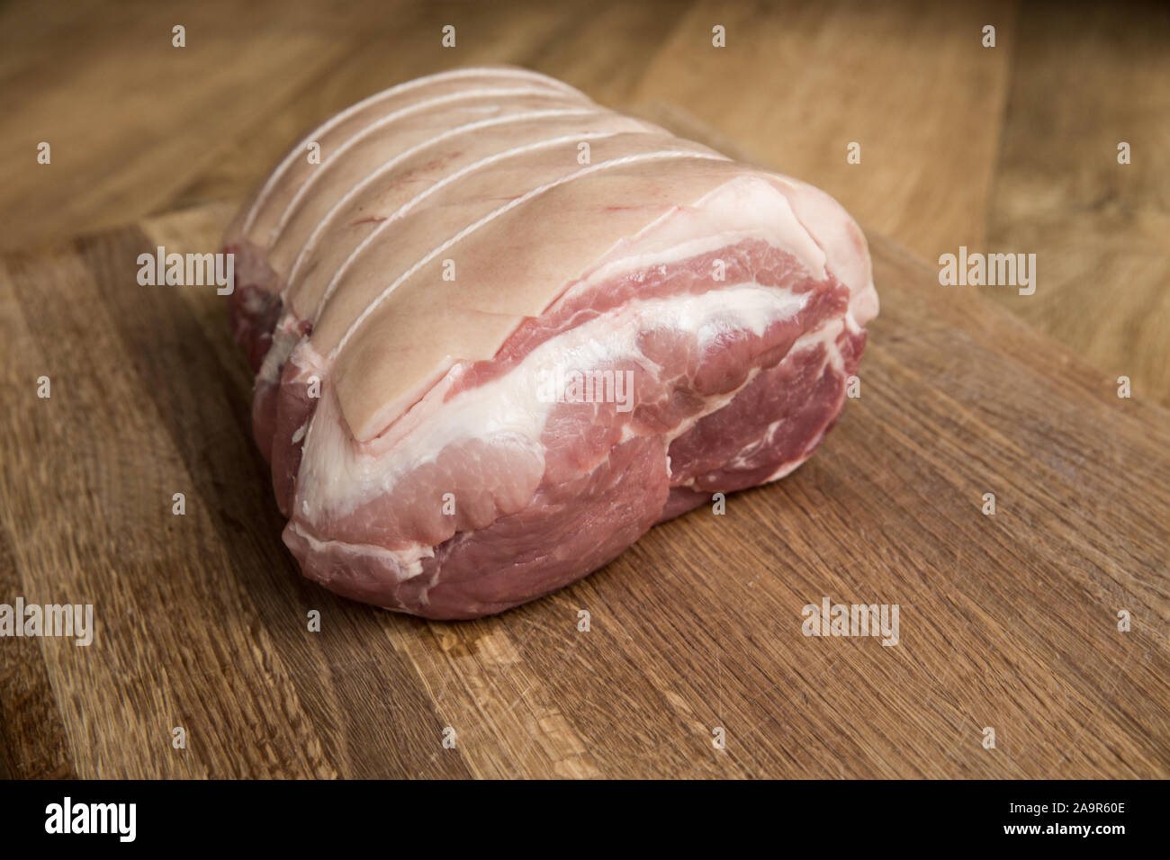 Una chiusura di un grezzo di taglio di carne chiamato una spalla di maiale legato e rullato con macelleria stringa con la sua pelle rigata pronto per il crepitio su una tavola di legno b Foto Stock
