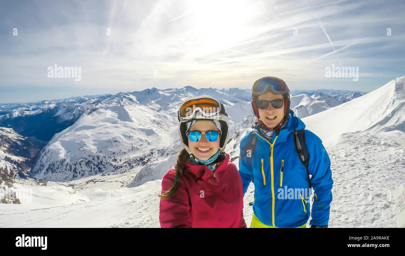 Un paio di sci outfits permanente sulla cima di una montagna innevata e godersi la giornata di sole. Entrambi sono ridendo e godendo della vista. Tall Foto Stock