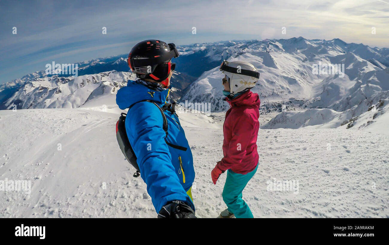 Un paio di sci outfits permanente sulla cima di una montagna innevata e godersi la giornata di sole. Entrambi sono ridendo e godendo della vista. Tall Foto Stock